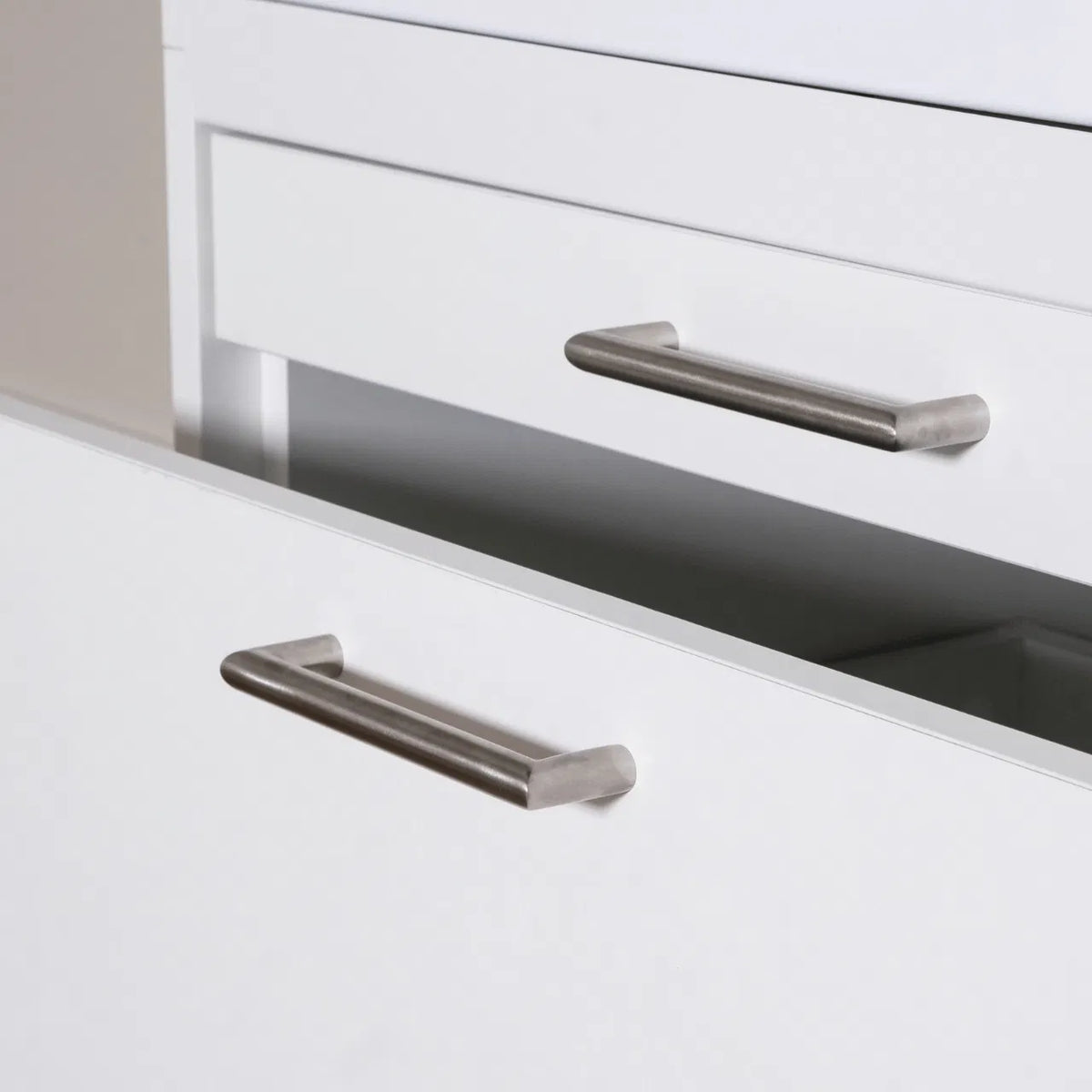 Matte silver metal cabinet handles with rounded edges on white drawers, modern minimalist style.
