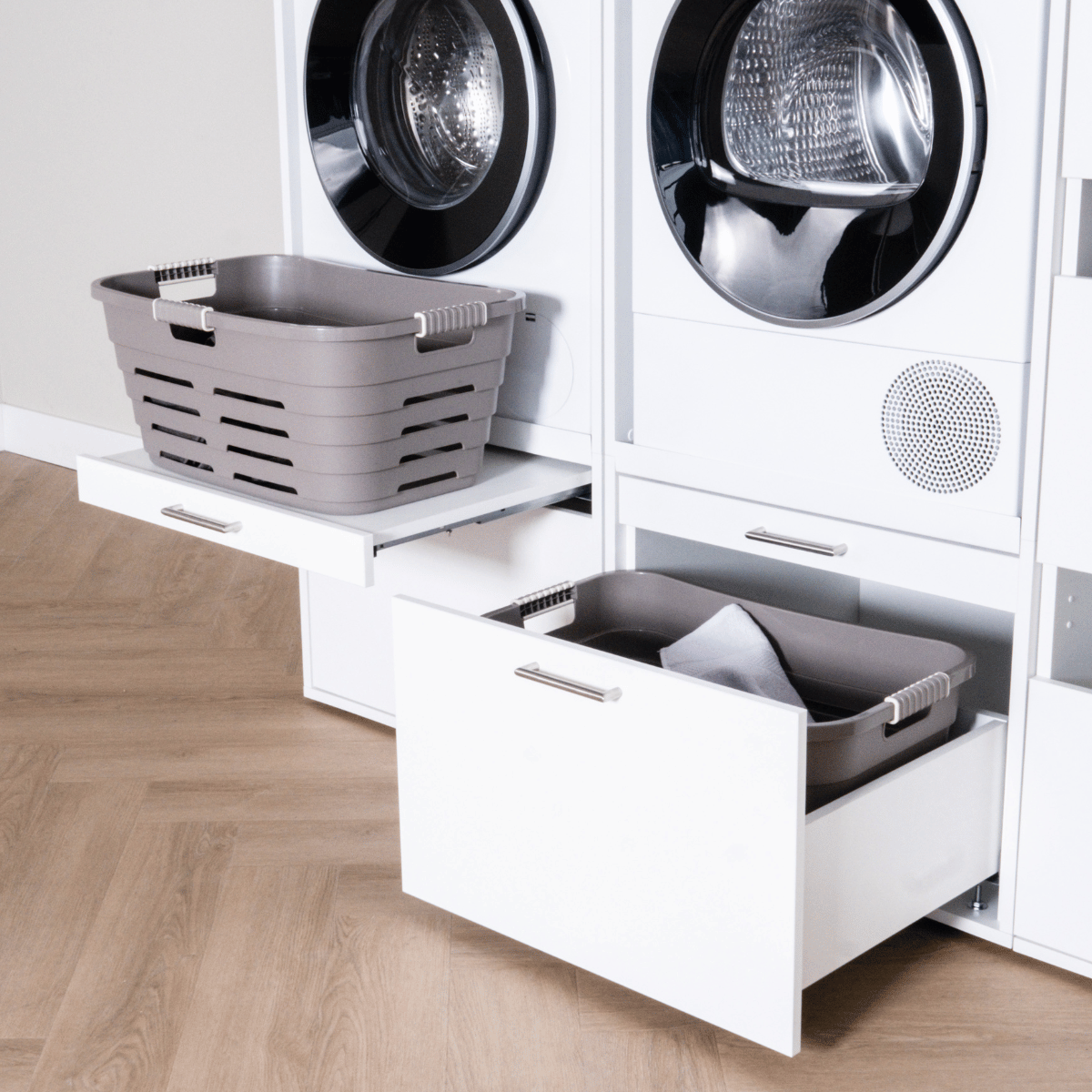 Modern white laundry cabinet with two pull-out drawers holding grey plastic laundry baskets.